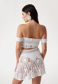 Witte gehaakte tweedelige set bestaande uit een strapless top en een minirokken met ingewikkelde patronen en uitsnijdingen.