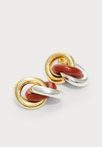 Boucles d'oreilles en métal doré et argenté avec des anneaux circulaires entrelacés et un accent en résine rouge. Fini brillant avec une texture lisse.
