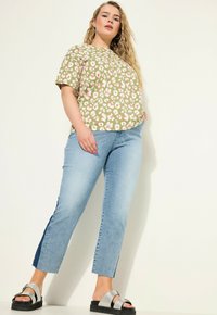 Zelená květinová potisková blůza s krátkým rukávem, spárovaná se světle modrými džínami po kotníky a stříbrnými sandály s tlustými černými podrážkami.