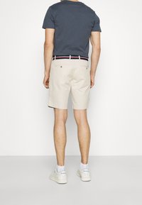 Vaaleat puuvillahousut rentoa mallia, joissa on tummansininen vyö punaisilla ja valkoisilla yksityiskohdilla, yhdistetty tummansiniseen T-paitaan ja valkoisiin lenkkarit.