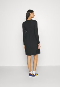 Czarna sukienka z długim rękawem, dopasowanym fasonem w górnej części i rozkloszowanym dołem, noszona z wielokolorowymi butami sportowymi z żółtymi paskami i logo.