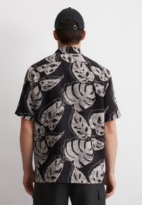 Schwarzes Kurzarmshirt mit weißem Blätterdruck, aus weichem Material und mit lockerer Passform, mit einem Kragen und geradem Saum.