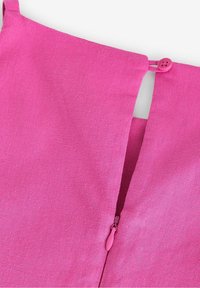 Gros plan sur un tissu rose vif montrant une fermeture éclair partiellement ouverte et une bride à bouton en haut.