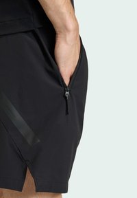 Čierne šortky s bočným zipsovým vreckom, vyrobené z ľahkého materiálu s jemným leskom a rozparkom na leme pre lepšiu pohyblivosť.