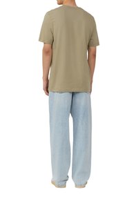 Olijfgroene t-shirt met korte mouwen en een ronde hals, gecombineerd met lichtblauwe wijde jeans met een subtiele textuur en een ontspannen pasvorm.