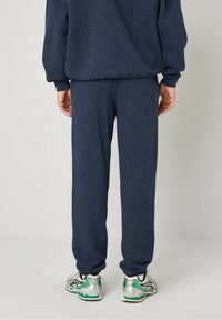 Navy blue sweatpants made of soft fabric with an elastic waistband and cuffs, paired with silver and green athletic shoes.