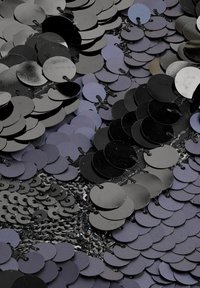 Czarne i metalicznie fioletowe okrągłe cekiny ułożone na teksturowanej tkaninie, w różnych rozmiarach i odcieniach, tworząc wizualnie dynamiczną powierzchnię.