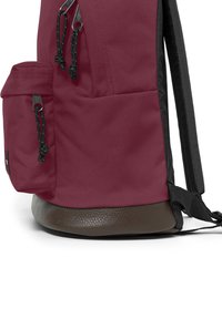 Mörk röd ryggsäck med en strukturerad mörkbrun bas, svarta remmar och en sidoficka med svarta dragsko och metalliska detaljer.