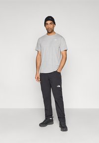 Γκρι κοντομάνικη μπλούζα με μικρό λογότυπο, μαύρο παντελόνι και μαύρα αθλητικά παπούτσια. Το μοντέλο φορά επίσης μαύρο ριμπ σκουφάκι. Απλή, καθημερινή εξωτερική ενδυμασία.