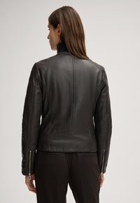 Schwarze Lederjacke mit schmaler Passform, strukturierten Schultern und Reißverschlussärmel. Glatte Oberfläche und dezente Steppnähte auf dem Rücken.