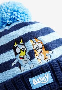 Gehaakte beanie met marineblauwe en lichtblauwe strepen, voorzien van een geborduurd ontwerp van twee cartoonhonden en een blauwe pompon bovenop.