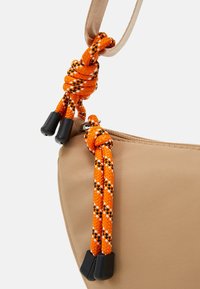 Borsa di tessuto beige con una texture liscia, dotata di dettagli in corda intrecciata arancione e nera e di accessori neri sui cursori della cerniera.