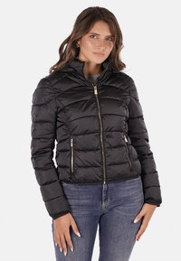 Giacca a vento nera con zip frontale, design trapuntato e due tasche laterali. Presenta dettagli in hardware dorato e una silhouette aderente.