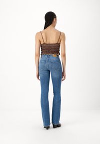 Hnědý crop top se smockovaným designem a tenkými ramínky spojený s modrými zvonovými džíny s vysokým pasem a zadními kapsami, pohled zezadu.