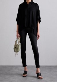 Camisa negra alargada con mangas cortas, combinada con jeans negros. Unas sandalias negras y un bolso verde claro completan el look.