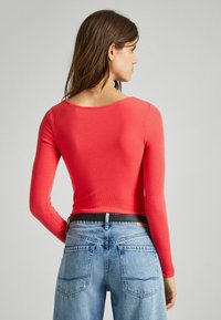 Maglia attillata a maniche lunghe in tessuto rigato di un vivace corallo, con un ampio scollo e abbinata a jeans in denim azzurro chiaro a vita alta.