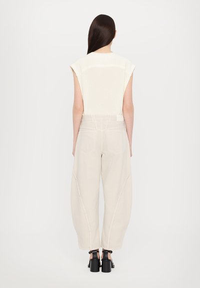 Oversized cream knit top with cap sleeves, paired with beige wide-leg trousers featuring diagonal seams and black platform sandals.
