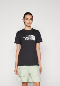 Must have musta t-särk mustast puuvillast, millel on valge "The North Face" logo. Mudel kannab helesiniseid cargo lühikesi pükse, millel on kaks esist taskut.