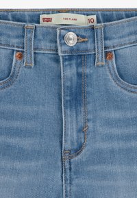 Pantalones vaqueros acampanados de mezclilla azul claro con textura suave, que cuentan con cierre de botón metálico, remaches de cobre y detalles de costuras en contraste.