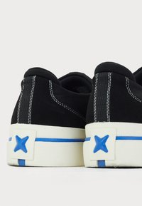 Black sneakers with white sole, blue accents, and stitched detailing. Features a textured back with a blue star-shaped emblem.