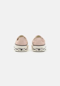 Light pink canvas sneakers with black and white rubber soles, featuring a star logo and classic low-top design. Accented with textured stitching.