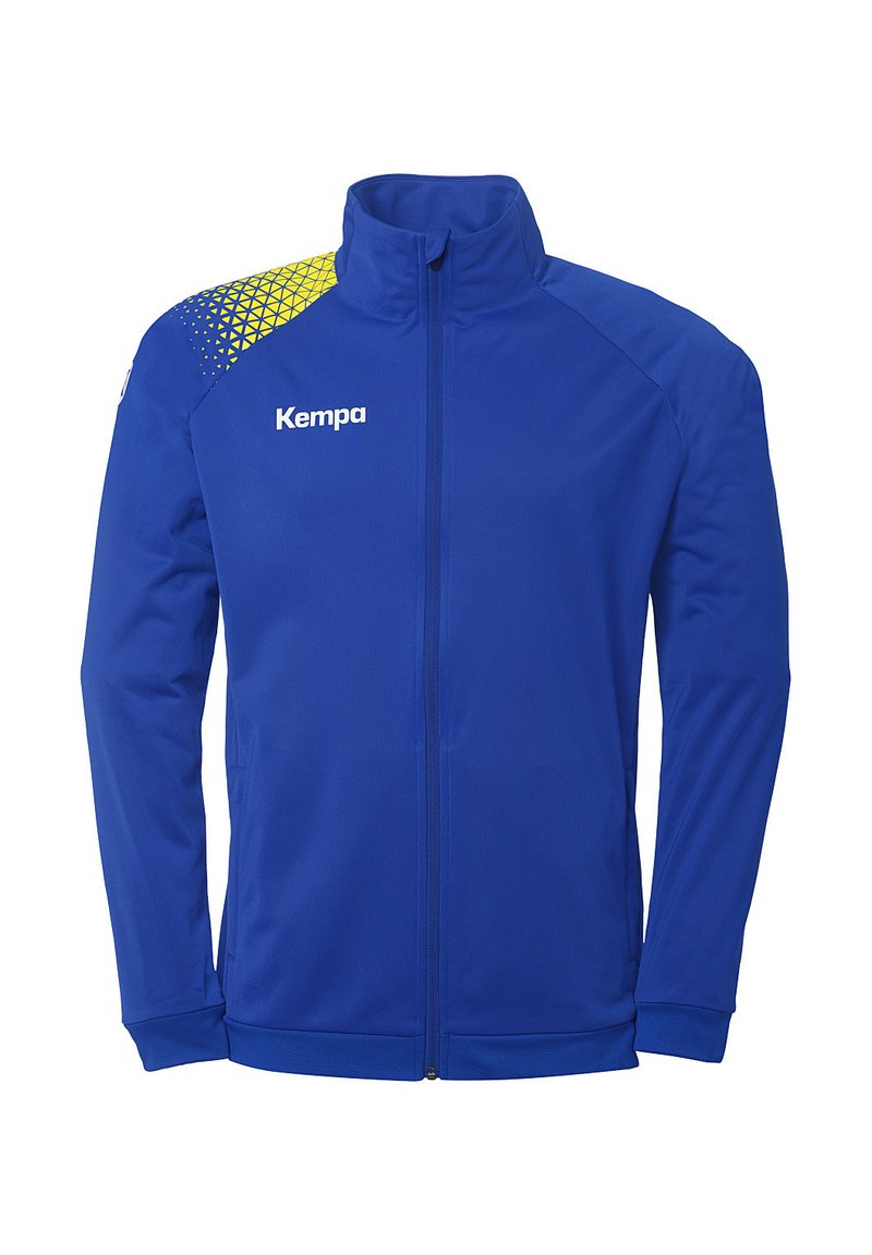 Veste de sport bleue avec un col montant, fermeture éclair à l'avant et un motif géométrique jaune et bleu sur l'épaule gauche. Nom de la marque "Kempa" affiché.