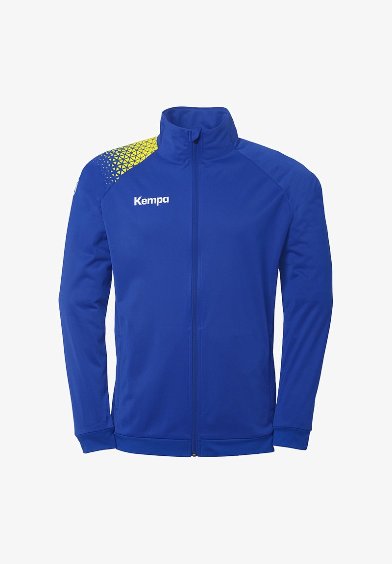 Veste de sport bleue avec un col montant, fermeture éclair à l'avant et un motif géométrique jaune et bleu sur l'épaule gauche. Nom de la marque "Kempa" affiché.