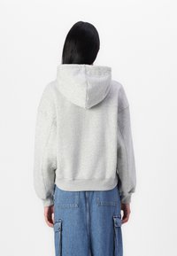 Sudadera con capucha gris de tela texturizada, de corte relajado y con dobladillo acanalado; combinada con pantalones holgados de estilo cargo en azul, que cuentan con bolsillos.