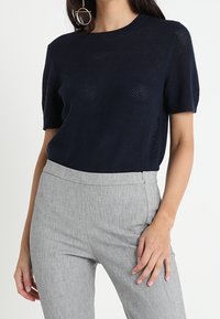 Haut en tricot bleu marine à manches courtes avec un col rond, présentant un motif texturé, associé à un pantalon gris clair ajusté.