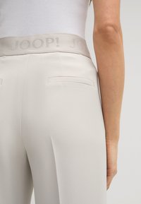 Hellgraue Hosen mit glatter Textur, elastischem Bund mit eingeprägtem Logo und zwei Gesäßtaschen.