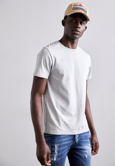 T-shirt en coton gris avec un col rond, associé à un jean en denim bleu déchiré. La casquette arbore un logo avec une base beige et des accents colorés.