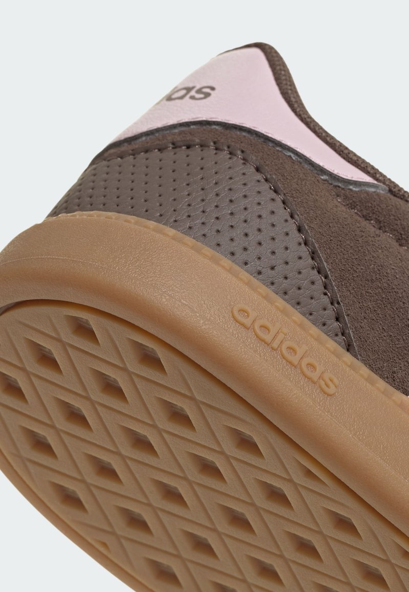 Brauner Sneaker mit strukturiertem Obermaterial, pinken Akzenten und einer Gummisohle mit Diamantmuster. Auf der Seite ist das Markenlogo zu sehen.