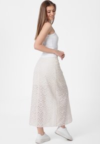 Maxi rok van doorschijnende lichtbeige stof met geometrische patronen, voorzien van een strakke tailleband en een vloeiende silhouet, gecombineerd met witte sneakers.