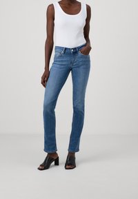 Blå denim jeans med rak passform, hög midja och fem fickor. Matchas med en vit linne och svarta klacksandaler.