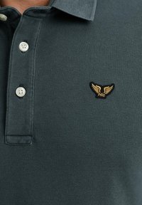 Polo shirt verde scuro con tessuto testurizzato, colletto classico e piccolo logo ricamato con ali in oro.