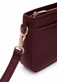Burgundy leather handbag with a smooth texture, featuring a gold-tone metal zipper, hardware, and a detachable strap.