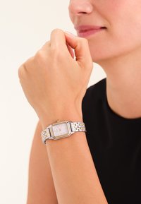 Orologio da polso rettangolare in tonalità argento e oro con cinturino texturizzato e quadrante bianco, caratterizzato da accenti minimalisti in oro.