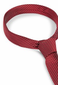 Röd mönstrad slips med diamantdesign, tillverkad av siden. Har en mjuk textur och är knuten runt halsen.