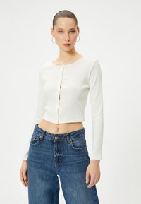 Witte geribbelde lange mouwen cropped top met een ronde halslijn en knoopsluiting, gecombineerd met high-waisted blauwe denim jeans.