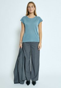 Gaiši zila īsām piedurknēm augšdaļa ar nelielu mirdzumu, apvienota ar pelēkiem platām kājām biksēm. Modelis tur atbilstošu pelēku žaketi.