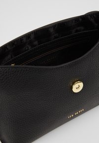 Černá kožená kabelka s texturovaným povrchem, zlatými kovovými prvky, magnetickým zapínáním a vnitřní kapsou na zip; uvnitř označena "TED BAKER".