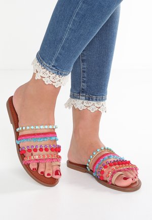 Płaskie sandały z wieloma kolorowymi paskami, ozdobione pomponami, koralikami i plecionymi detalami. Brązowa podeszwa o gładkim wykończeniu.