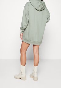 Mátová oversized mikina s kapucí na šňůrku, manžetami a lemem, doplněná off-white kotníkovými botami s robustním podpatkem.