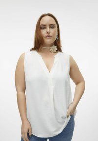 Haut sans manches blanc avec un décolleté en V, en tissu texturé et à la coupe ample. Associé à un léger collier ras du cou avec un accent floral.