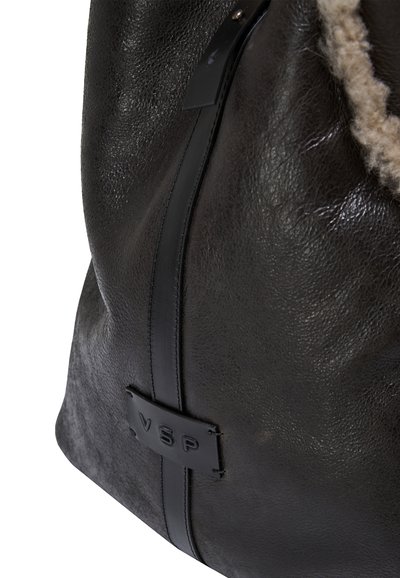 Borsa nera in pelle con una consistenza morbida, caratterizzata da una forma liscia e arrotondata e un accento del logo ben visibile su un lato.