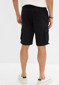 Pantaloni cargo neri in cotone. Caratterizzati da tasche laterali e posteriori, vita elastica e vestibilità comoda. Indossati con scarpe da ginnastica bianche.