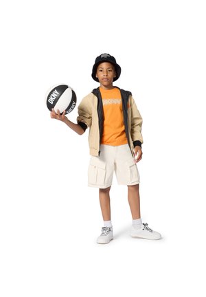 Jongen met emmerhoed, beige jas, oranje DKNY-shirt, cargoshort, houdend een zwart-witte DKNY basketbal.
