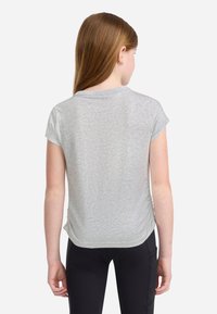 T-shirt grigio a maniche corte con scollatura rotonda, texture morbida e orlo leggermente curvo. Indossato con pantaloni sportivi neri.