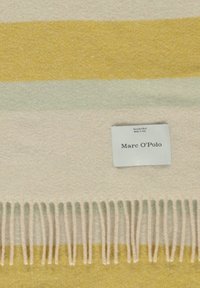 Écharpe en laine douce aux rayures jaunes, vert clair et beige, bordure frangée, avec une étiquette de marque Marc O'Polo blanche.
