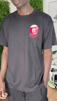Juodas medvilninis marškinėliai su apvalia daugiaspalve grafika, kurioje yra adidas logotipas, trumpomis rankovėmis, apvaliu kaklu ir laisvu siluetu.